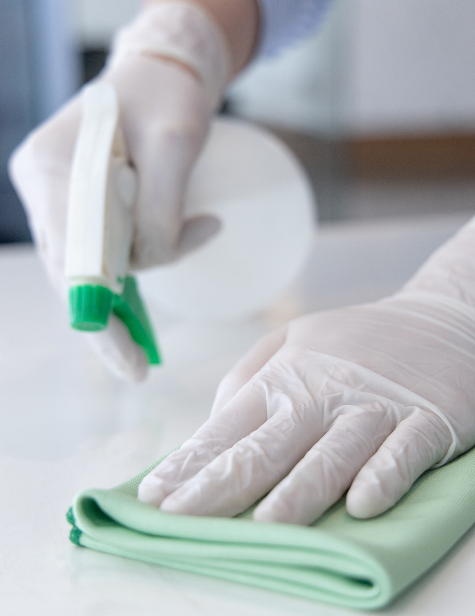 Gloved hands sanitizing a countertop with a green microfiber cloth